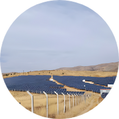 Aerial view of a circular solar farm surrounded by a fence, showcasing rows of solar panels.